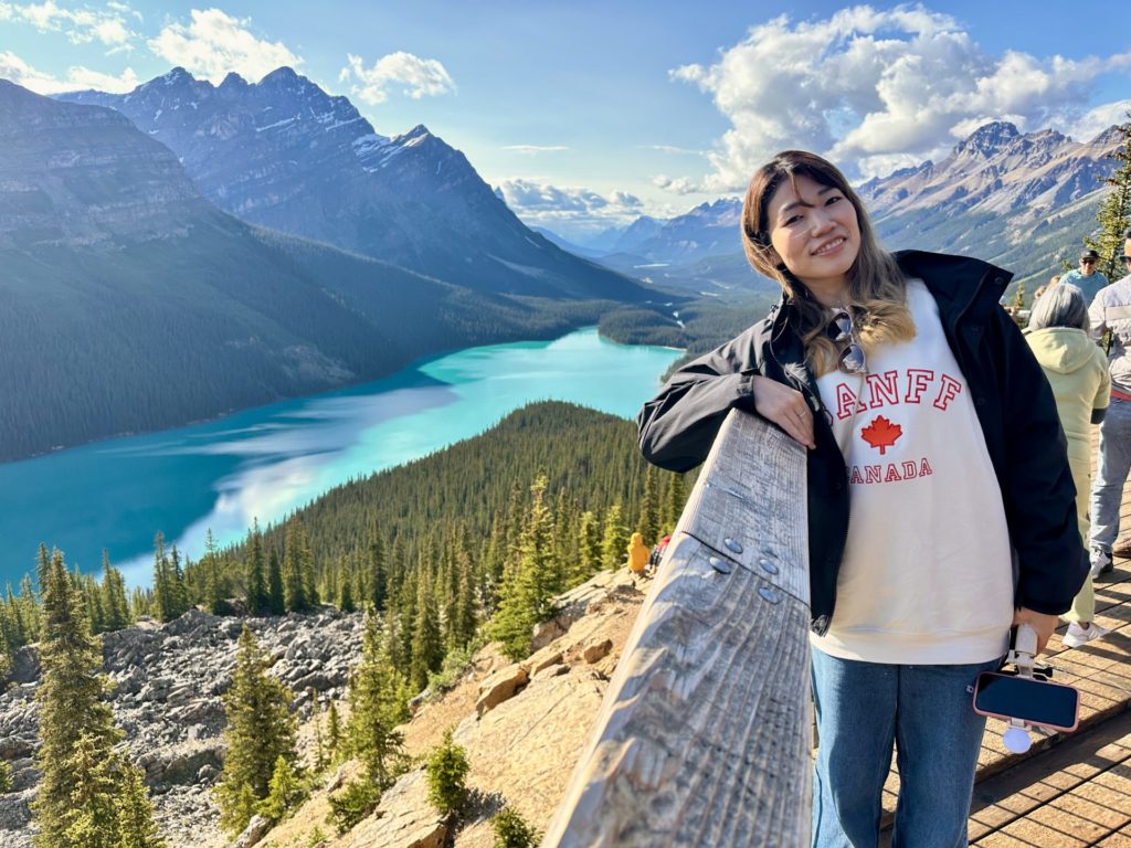 カナダ・バンフ国立公園にあるペイト湖の絶景を背景に笑顔で立つ言い出しっぺ